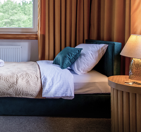 Przytulny pokój z pojedynczym łóżkiem, poduszkami, zasłonami i lampką nocną przy oknie