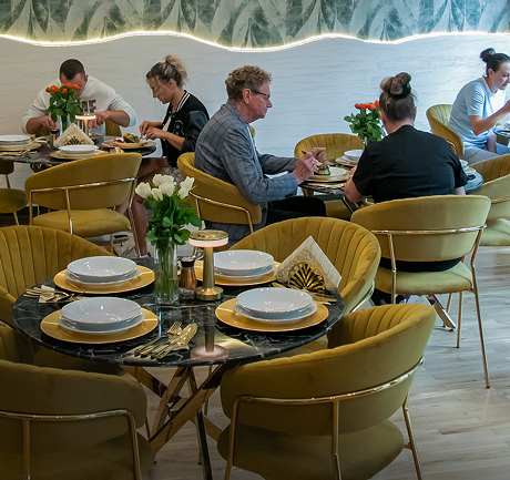 Sala jadalni z elegancko nakrytymi stołami i gośćmi podczas posiłku, złote krzesła i dekoracje z kwiatami