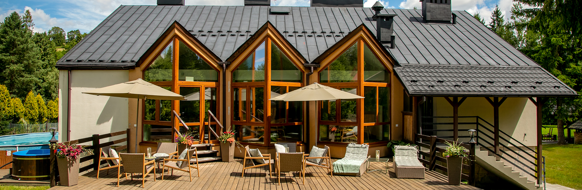 Taras ośrodka Cisza z dużymi przeszkleniami, stolikami i leżakami pod parasolami w otoczeniu zieleni