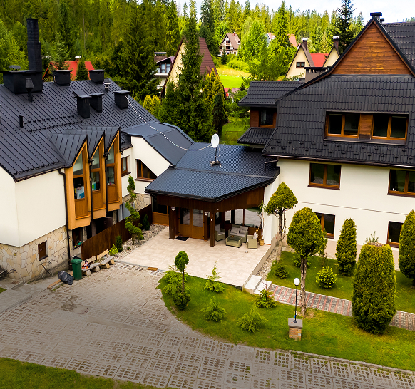 Widok z góry na budynek ośrodka Cisza i zielony ogród z podjazdem, w tle las i zabudowa górska