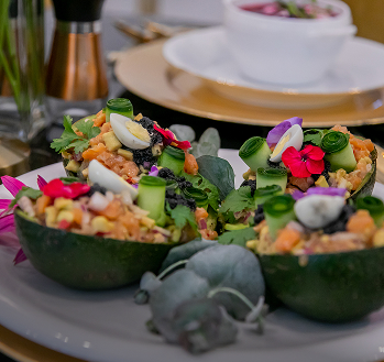 Przystawka podana w połówkach awokado z warzywami, ziołami i jadalnymi kwiatami na talerzu