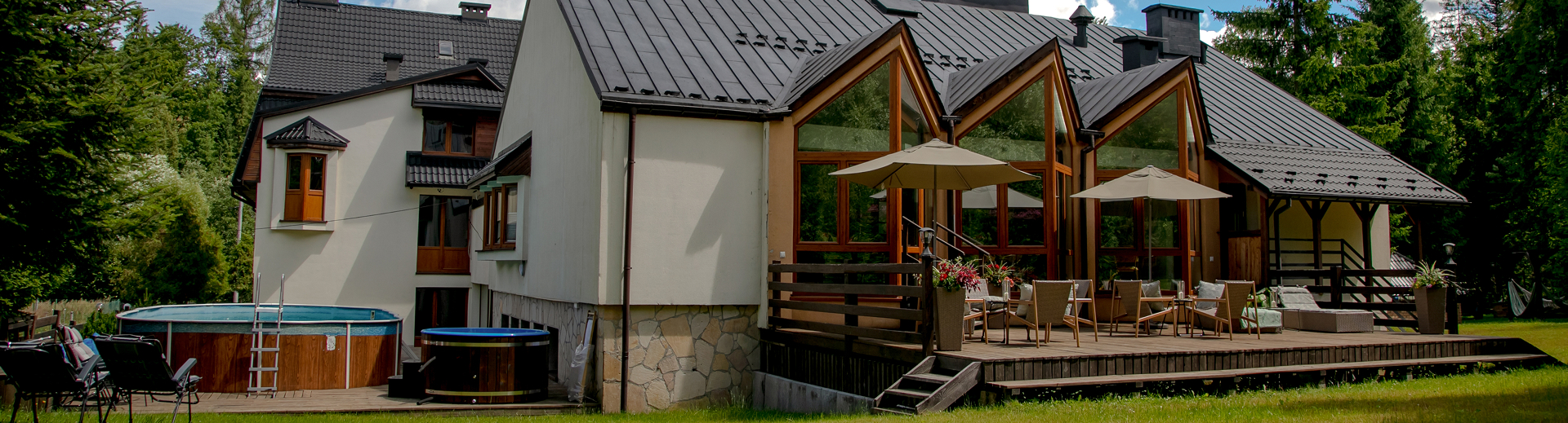 Budynek ośrodka Cisza z dużymi przeszkleniami i tarasem wypoczynkowym, obok balia i basen w otoczeniu lasu