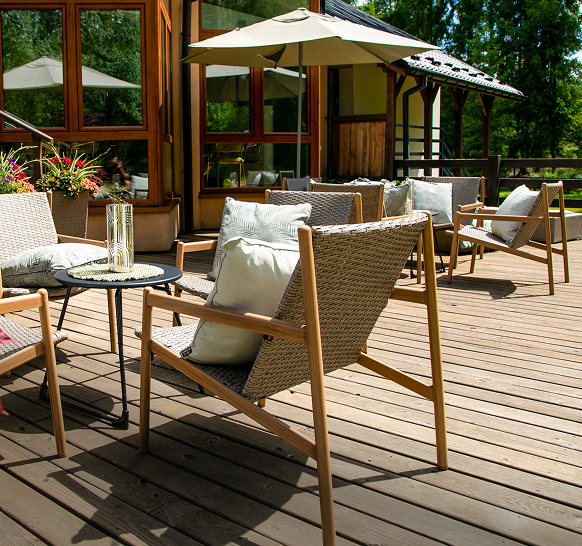 Strefa relaksu na drewnianym tarasie z wygodnymi fotelami, poduszkami i parasolem w otoczeniu zieleni