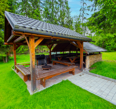 Zadaszona altana z miejscem na grilla i ławami w zielonym ogrodzie ośrodka Cisza